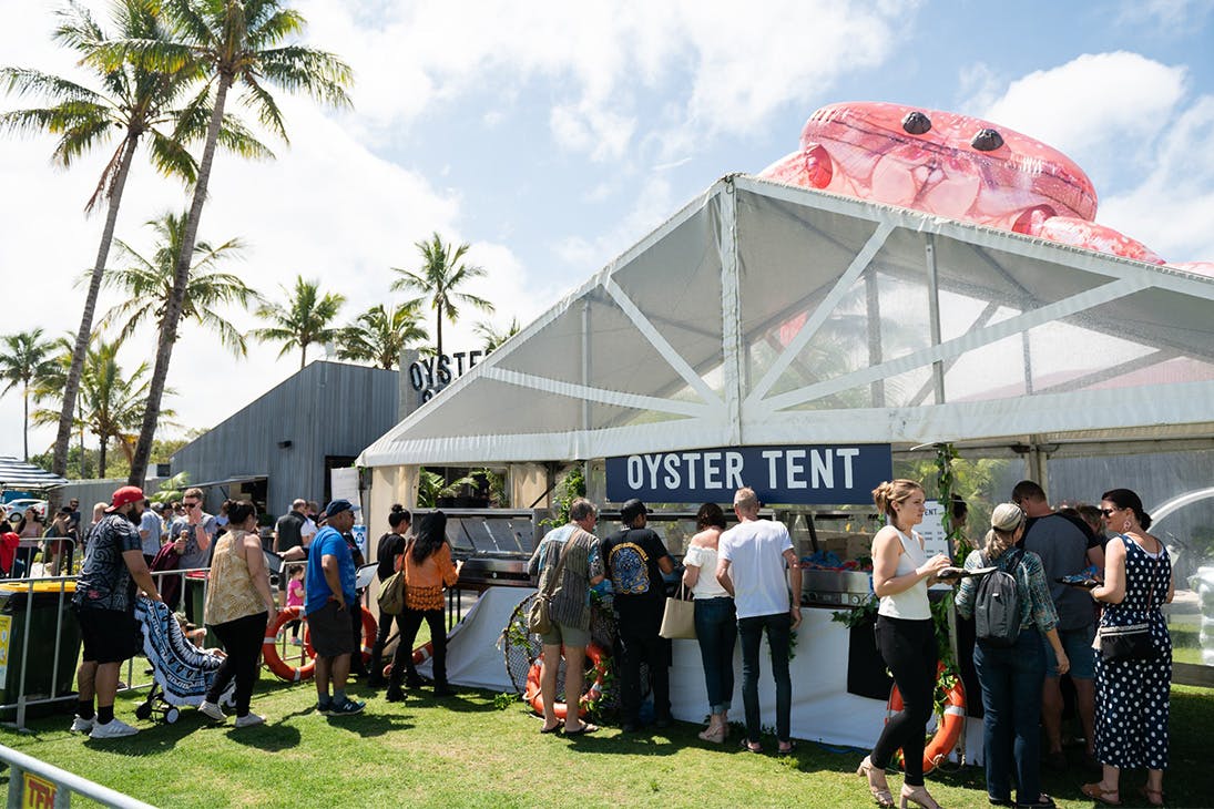 a large white tent that says 'oyster tent' with a queue of people outside it